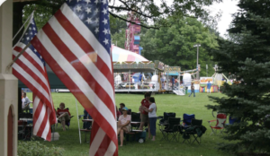 2 American flags hanging in front of people in a park